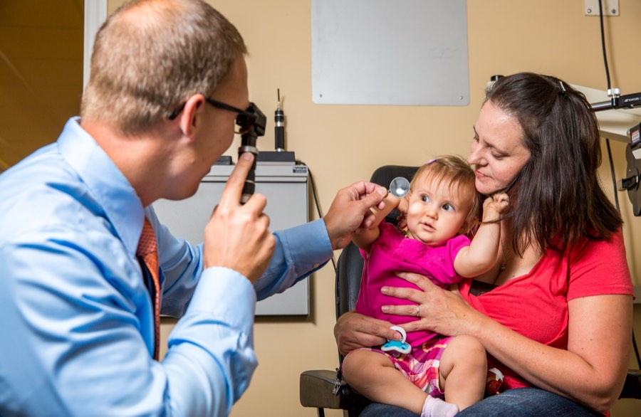 Dr. Thomas examining an infant sitting on her mother's lap